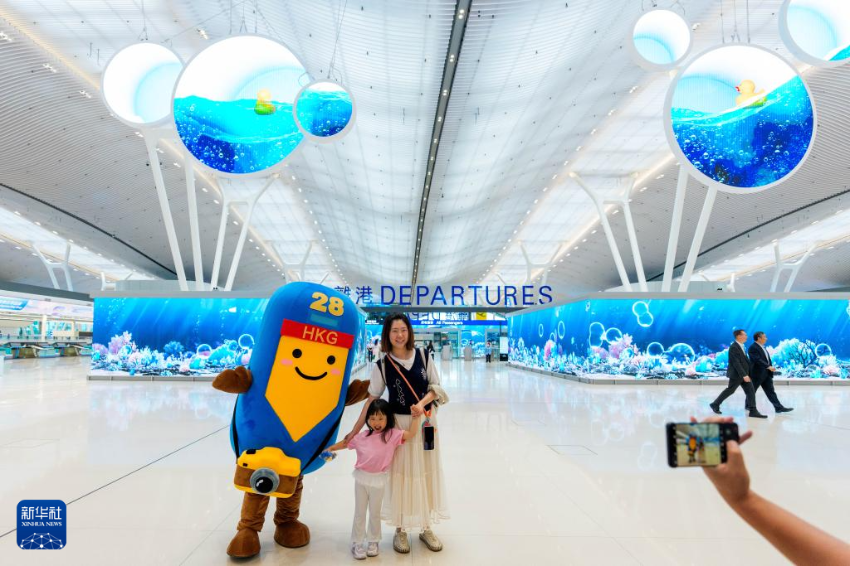 5月27日，旅客在香港国际机场二号客运大楼离境大堂与机场吉祥物合影。