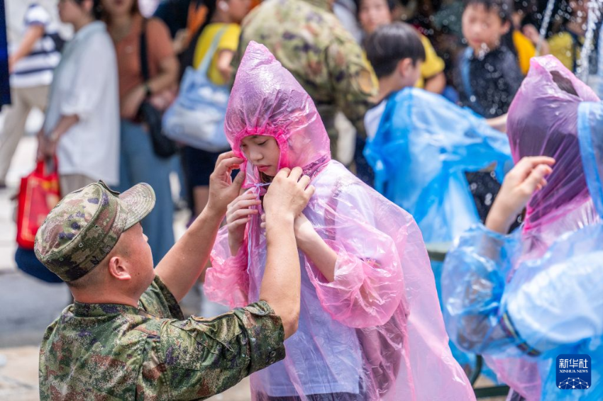 6月20日，一名士兵为军营开放活动上学习体验管路包扎操作的学生整理雨衣。