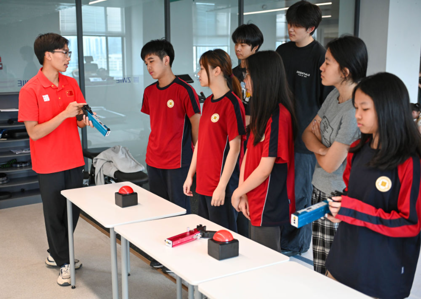 ↑图为广东现代五项运动协会教练员滕泽华（左一）为广州市中黄港澳子弟学校学生讲解射击注意事项（6月19日摄）。