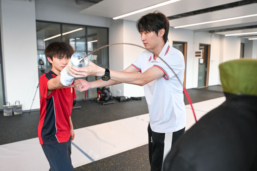 ↑图为广东现代五项运动协会教练员肖勇炫（右）纠正广州市中黄港澳子弟学校港籍生张嗣涛击剑技术细节（6月19日摄）。