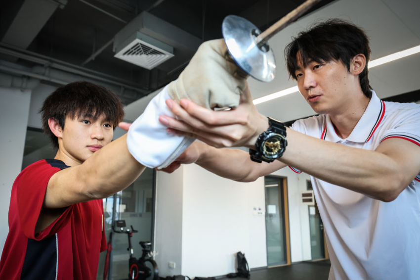 ↑图为广东现代五项运动协会教练员肖勇炫（右）纠正广州市中黄港澳子弟学校港籍生张嗣涛击剑技术细节（6月19日摄）。
