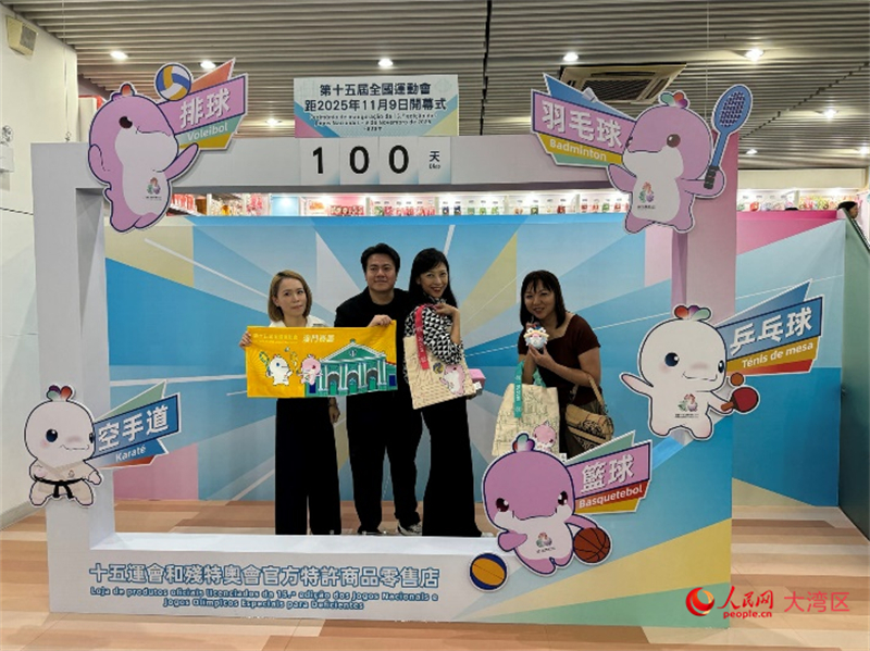 图为特许商品零售店顾客与十五运会开幕倒计时牌合影。
